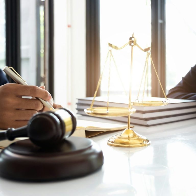 Martillo de juez y balanza sobre una mesa, con personas en un entorno legal.