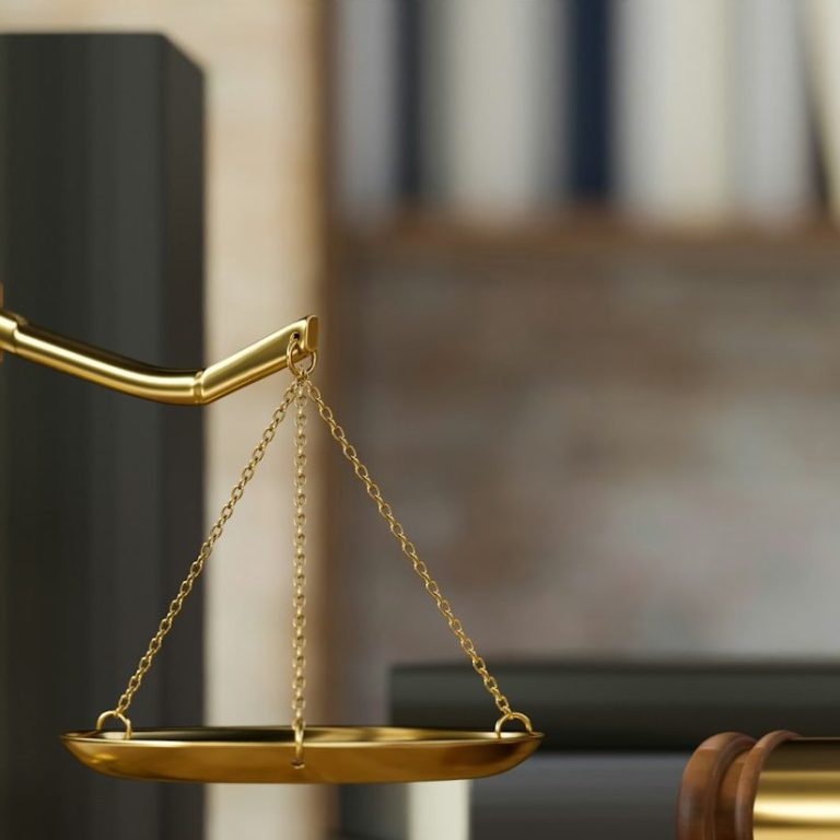 Balanza de la justicia junto a libros y un mazo sobre una mesa de madera.
