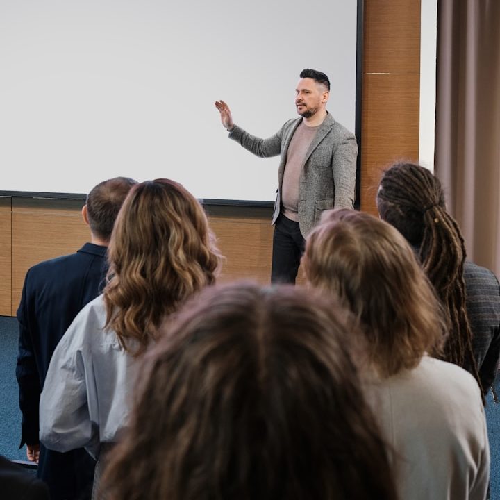 Hombre presentando en una sala a un grupo de personas sentadas.